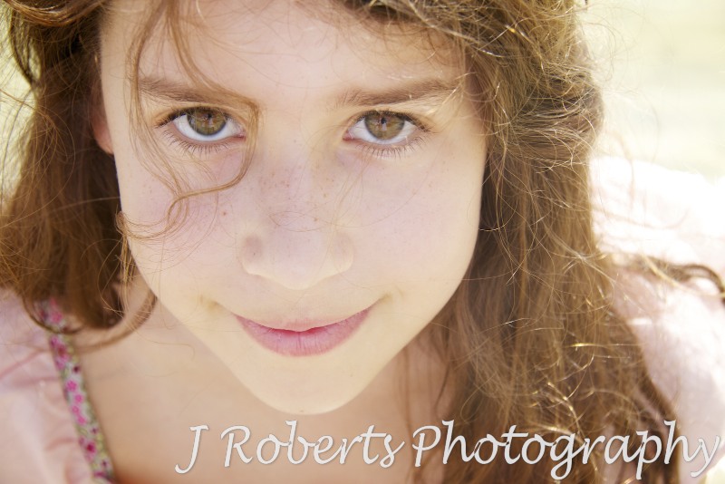 Young girl smiling up at the camera through stray hair - family portrait photography sydney